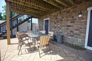 An outdoor patio with a stone floor, a wooden pergola, a table with chairs, and a stone wall. - Welcome to The Captain and Crew Quarters on Anchor Drive at Apple Valley Lake! (Howard)