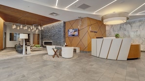 Un espace d’accueil moderne, doté d’un comptoir de réception en bois, d’un mur décoratif en pierre et d’un coin salon avec des canapés et une table basse.
