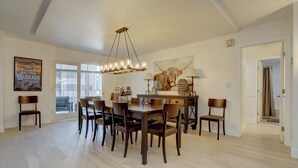 Un coin repas avec une table et des chaises en bois, un lustre et un grand tableau représentant un taureau accroché au mur.