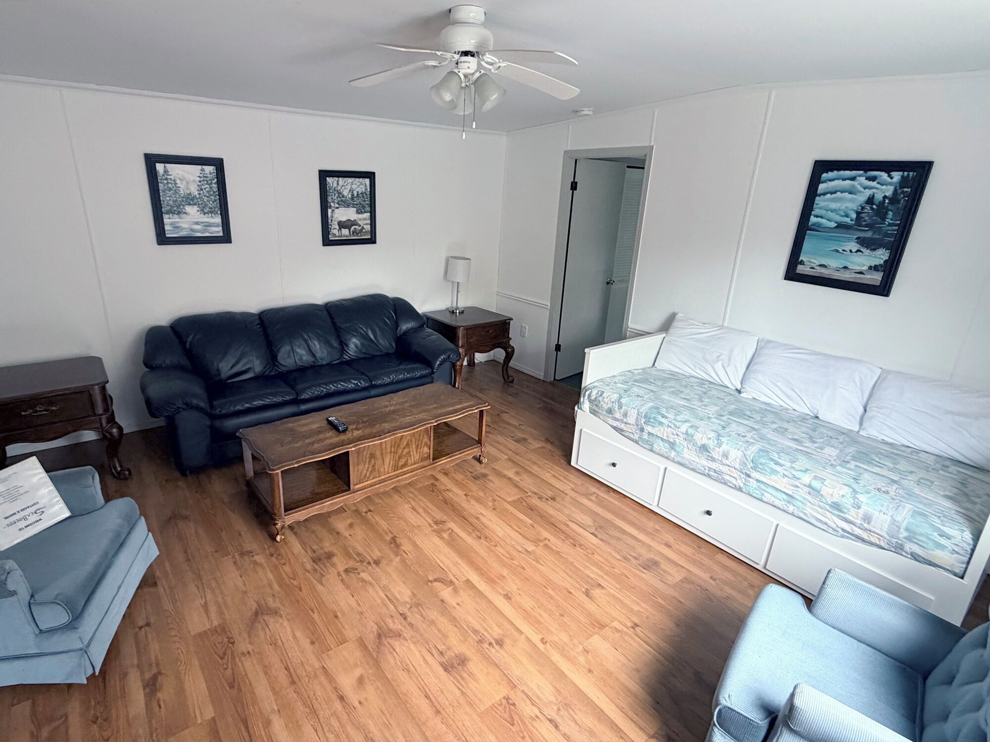 A living room with a sofa, a coffee table, a bed, and a ceiling fan.