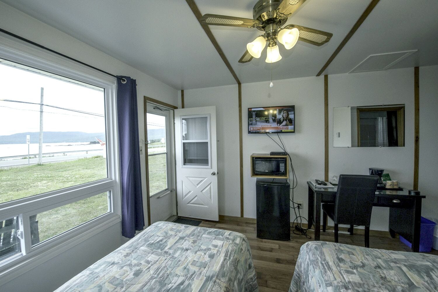 A hotel room with two beds, a desk with a computer, a TV, and a ceiling fan.