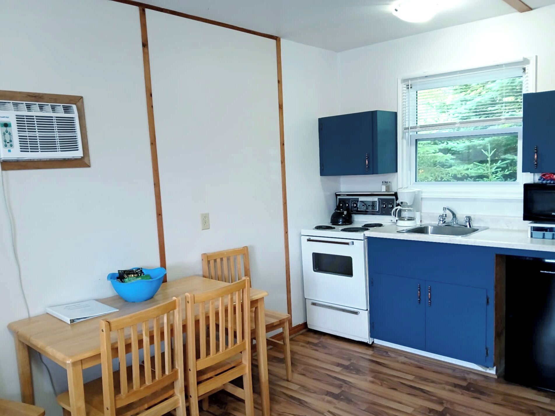 A compact kitchen with a dining table, chairs, a microwave, stove, and cabinets.
