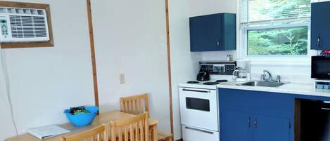 A compact kitchen with a dining table, chairs, a microwave, stove, and cabinets.