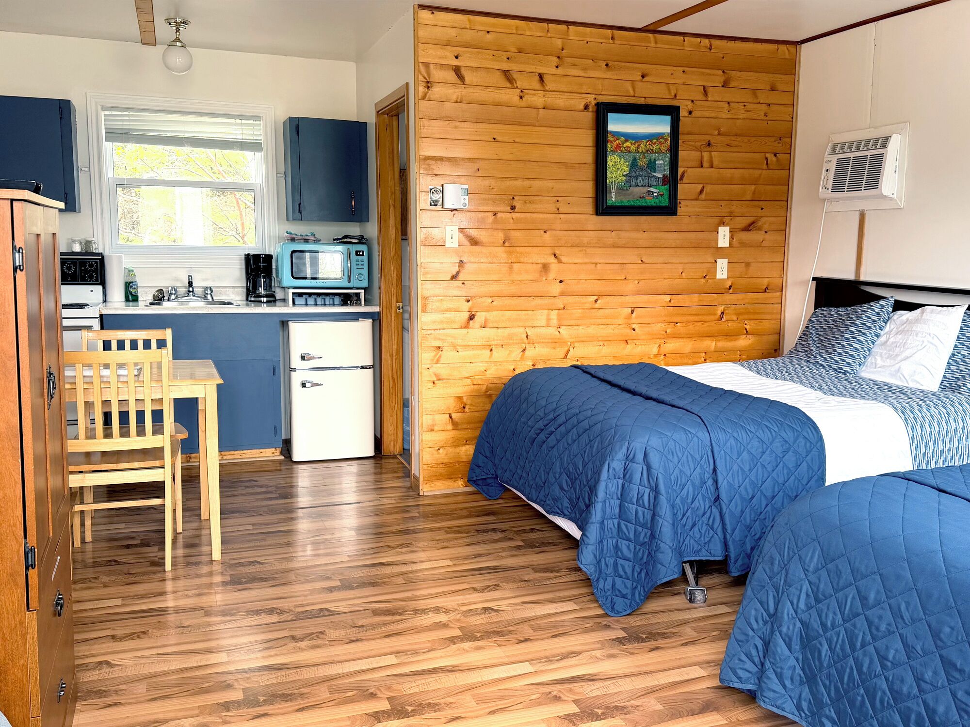 A compact room with a bed, a small kitchenette, and a wooden wall.