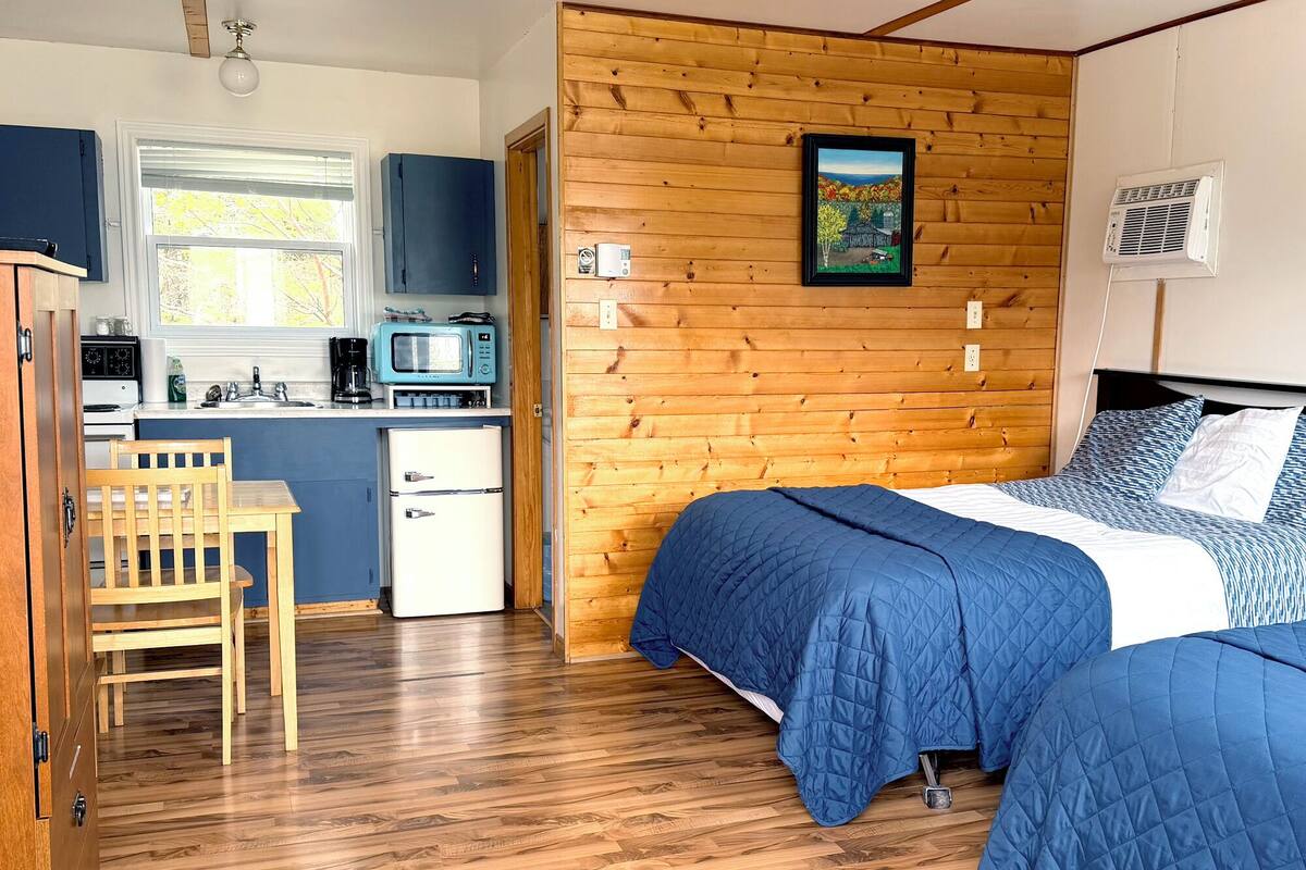 Een knus kamertje met een bed, een kleine kitchenette en een houten wand.