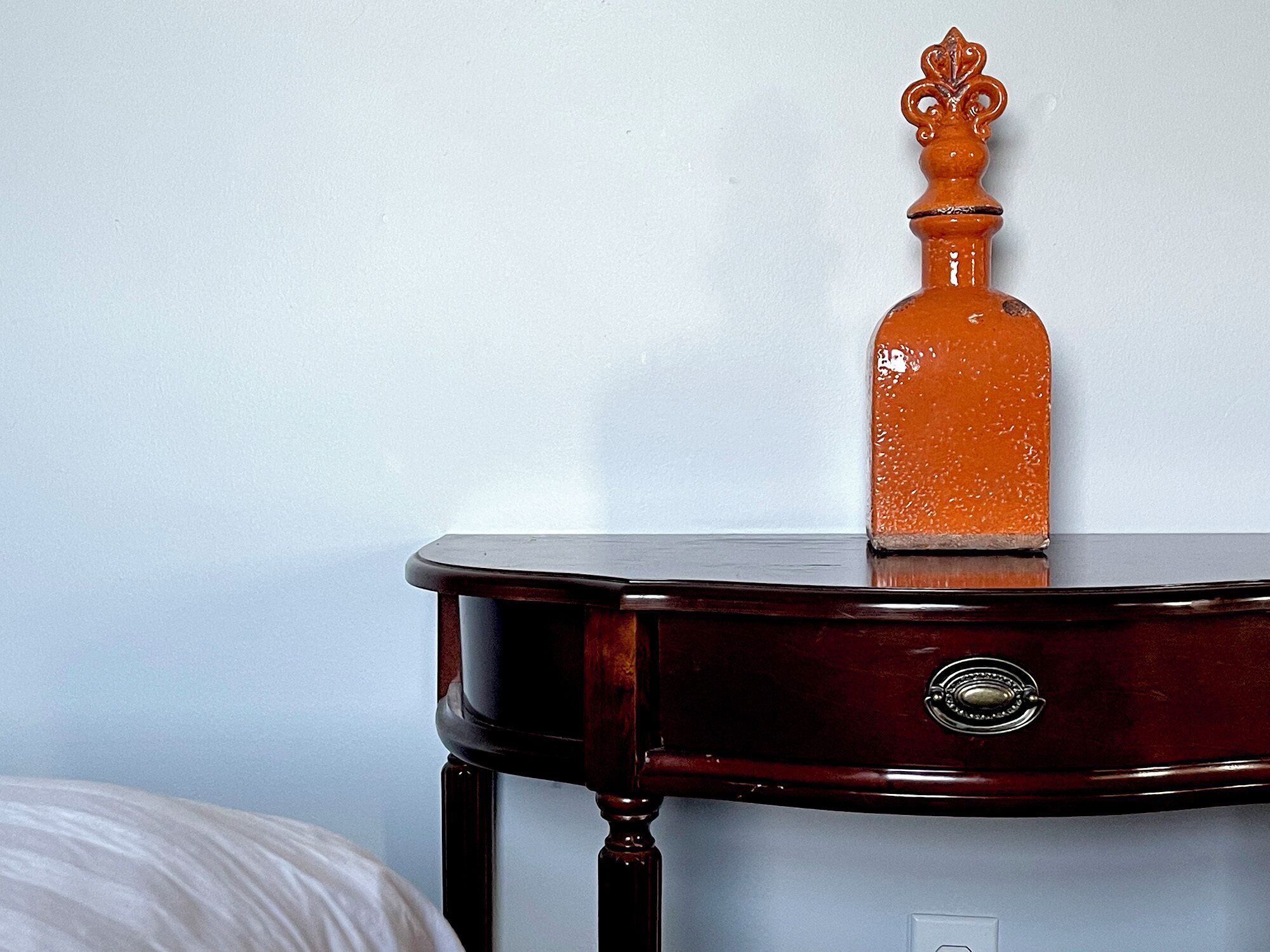 A wooden side table with a drawer and a decorative bottle on top.
