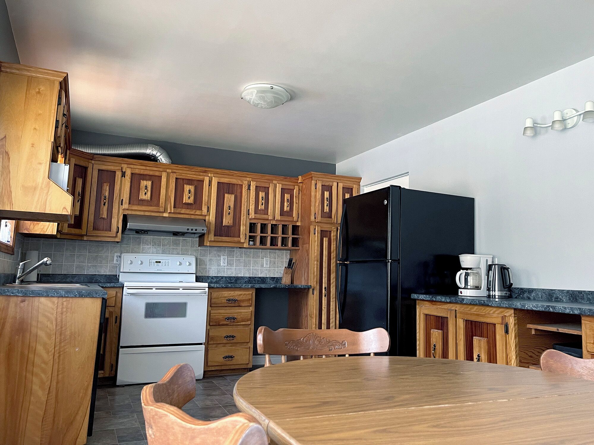 Une cuisine avec des meubles de rangement en bois, un réfrigérateur noir, une cuisinière et une table à manger avec des chaises.