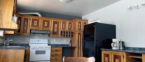 Une cuisine avec des meubles de rangement en bois, un réfrigérateur noir, une cuisinière et une table à manger avec des chaises.