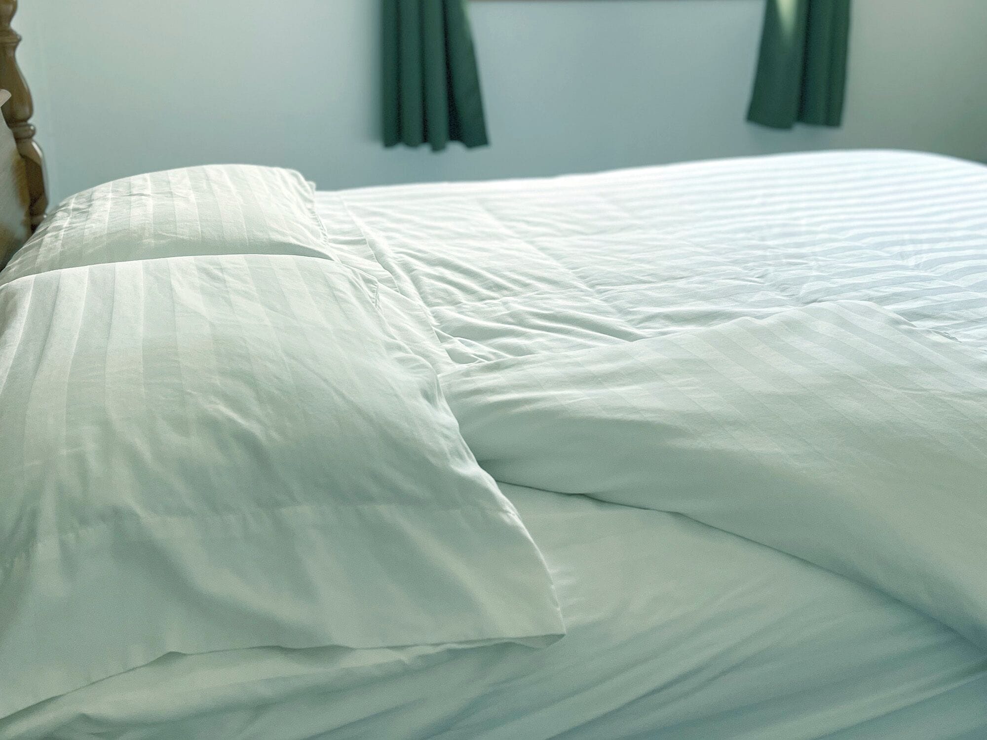 Un lit bien fait, avec du linge de lit blanc et une tête de lit en bois.