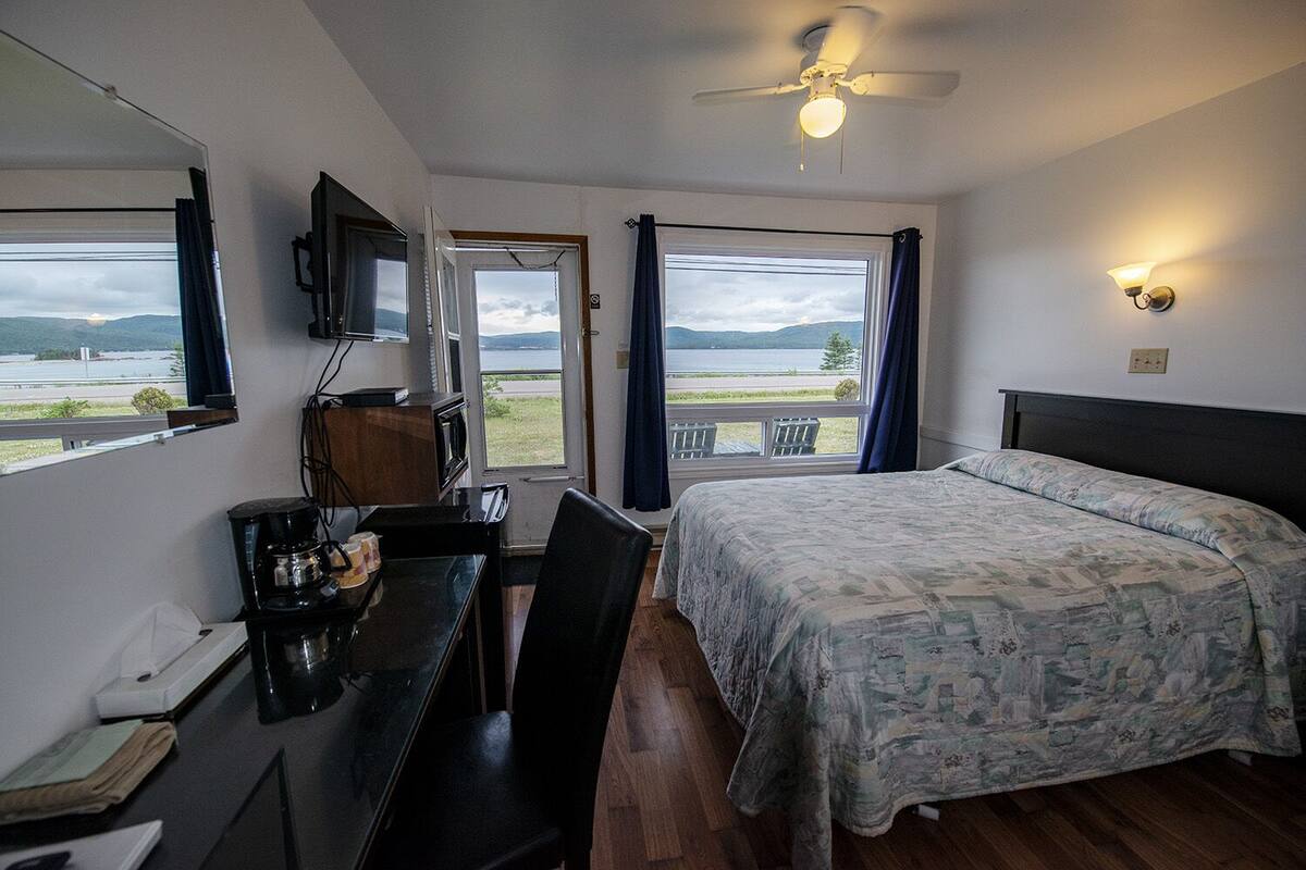 Een slaapkamer met een bed, een bureau, een stoel, een televisietoestel en uitzicht op een meer.