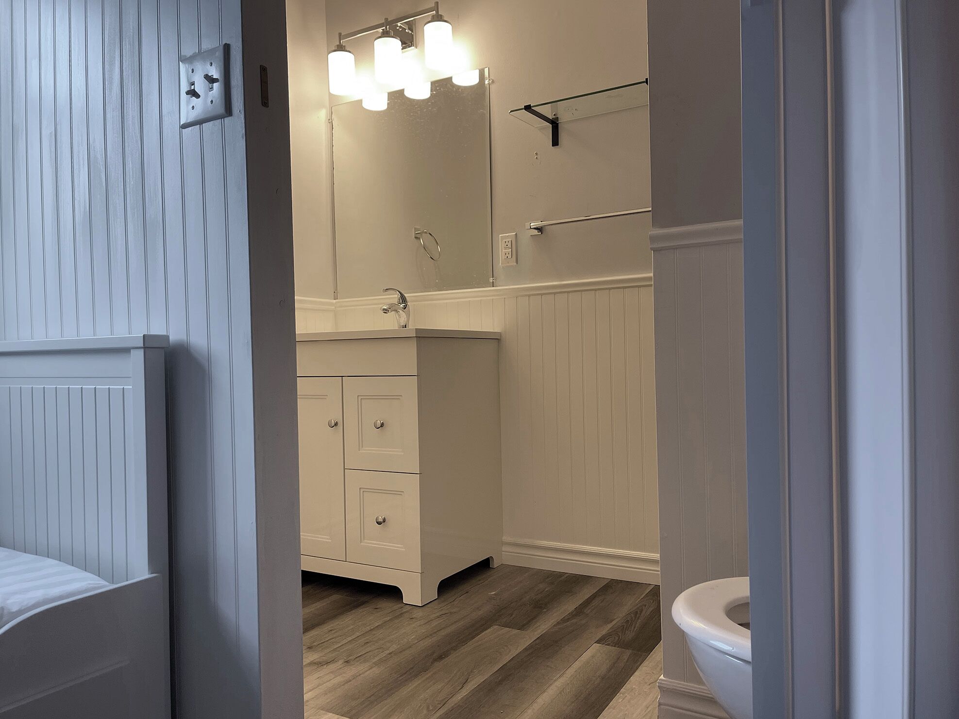 A bathroom with a white vanity, a mirror, a towel rack, and a toilet.