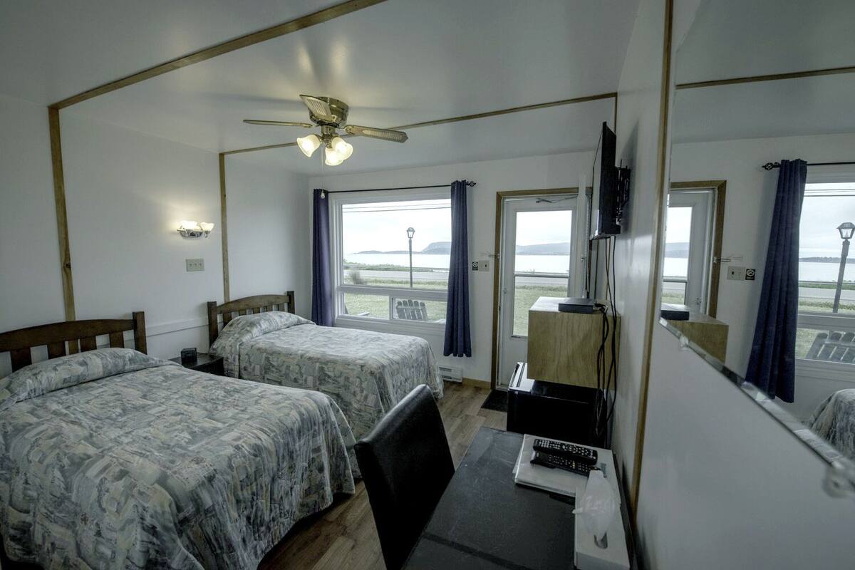Hotelkamer met twee bedden, een plafondventilator, een televisie en uitzicht op zee.