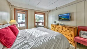 Una camera da letto con un letto, una cassettiera, una televisione e due finestre.