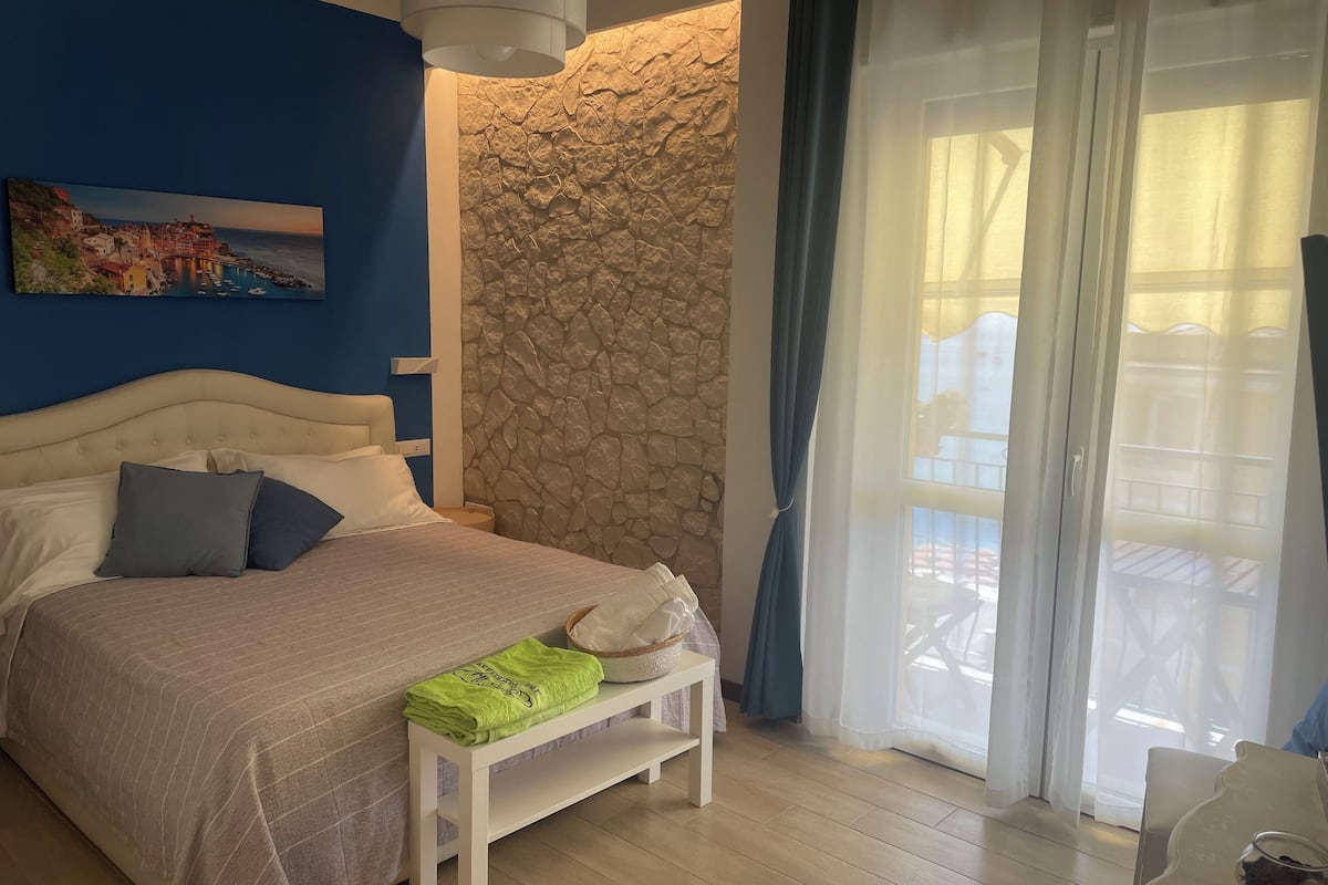 Un dormitorio con cama, un muro decorativo de piedra, una ventana con cortinas y un cuadro en la pared.