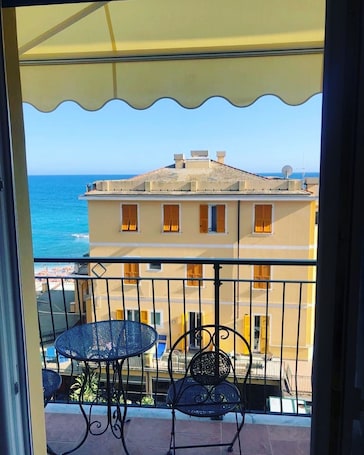 A balcony with a table and chairs, overlooking a building and the sea.