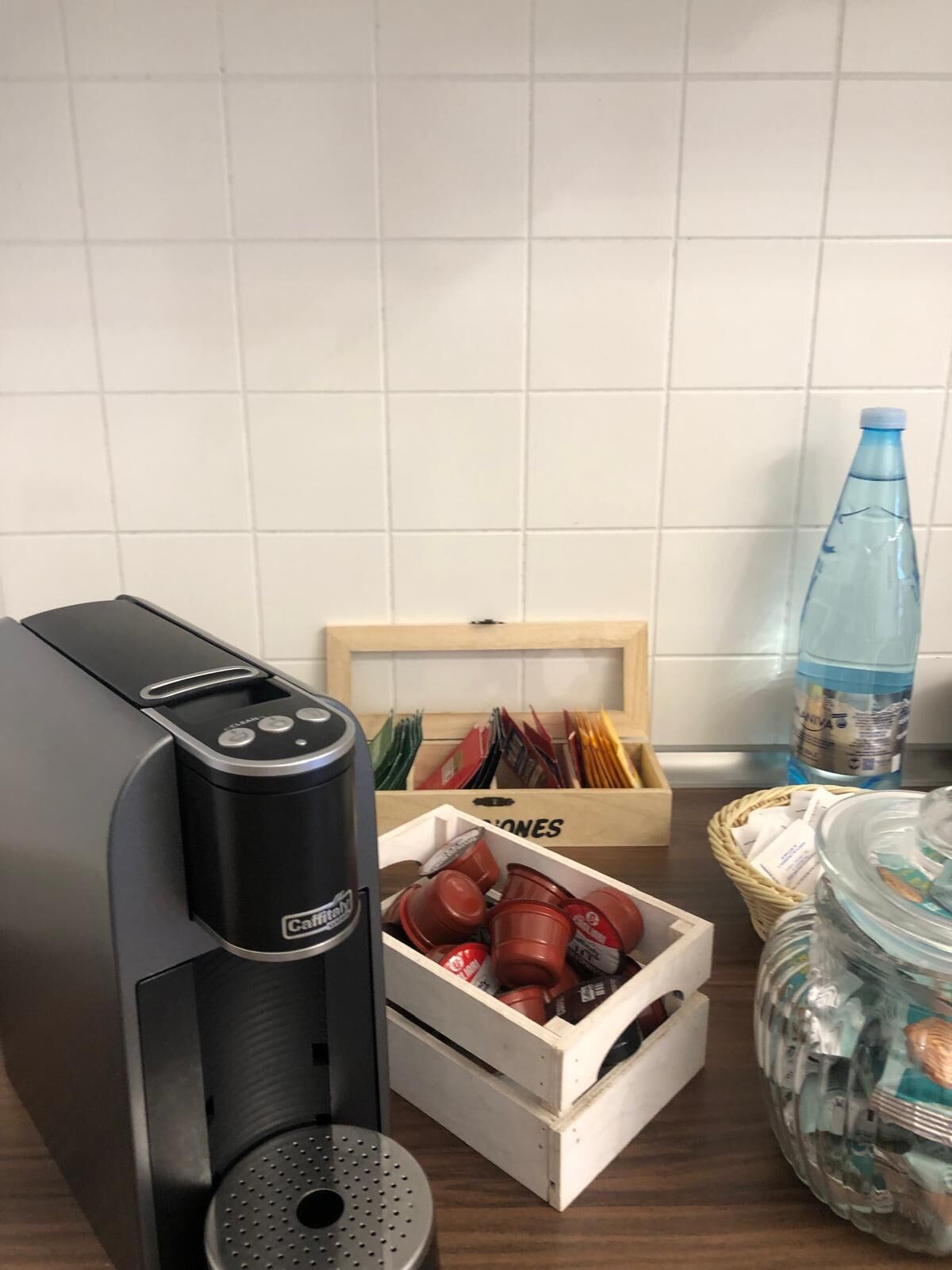 Une cuisine équipée d’une machine à café, d’une boîte en bois contenant des objets rouges et d’une bouteille d’eau.