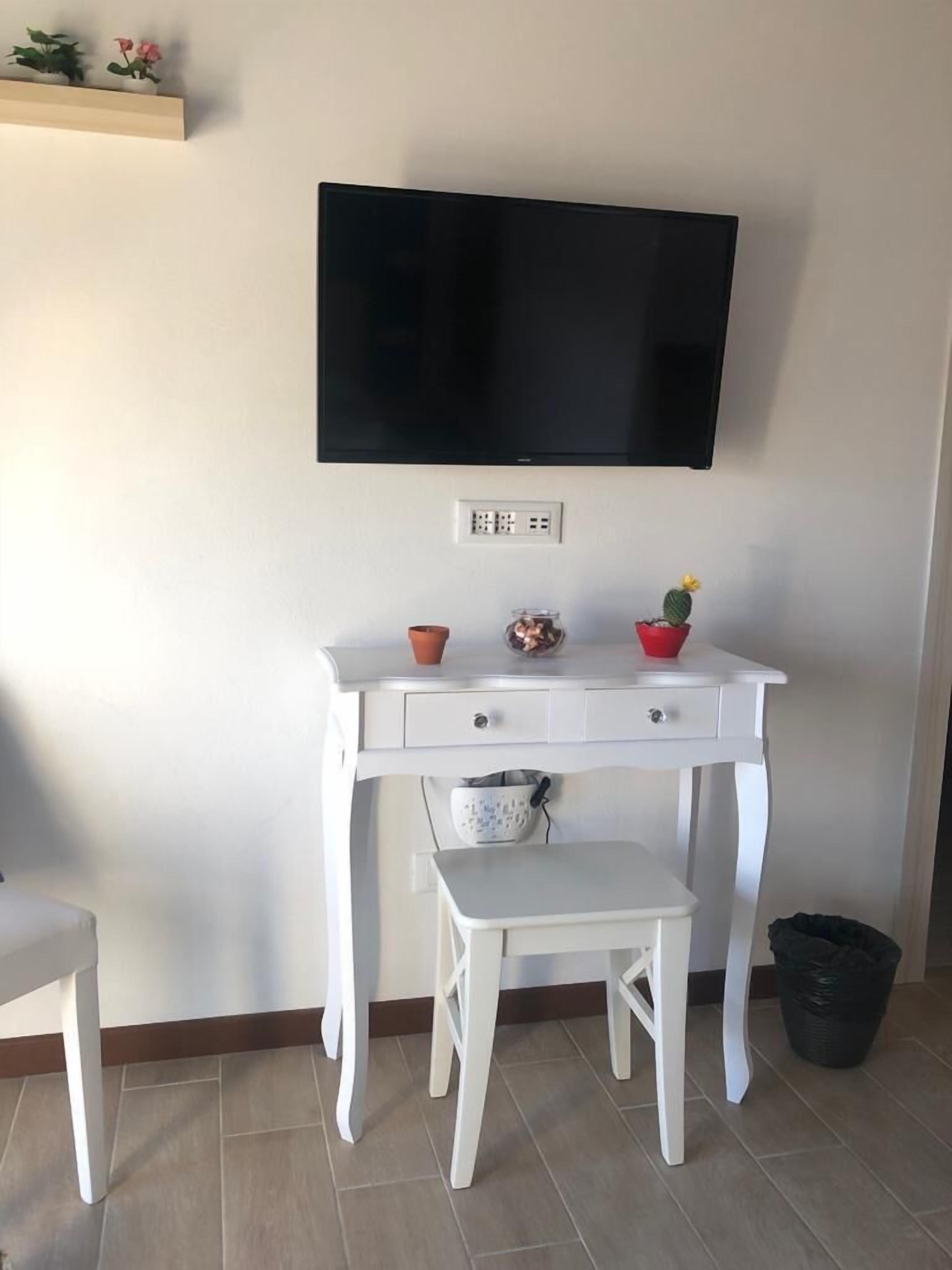 A white desk with a television mounted above it, a small potted plant, and a trash bin.