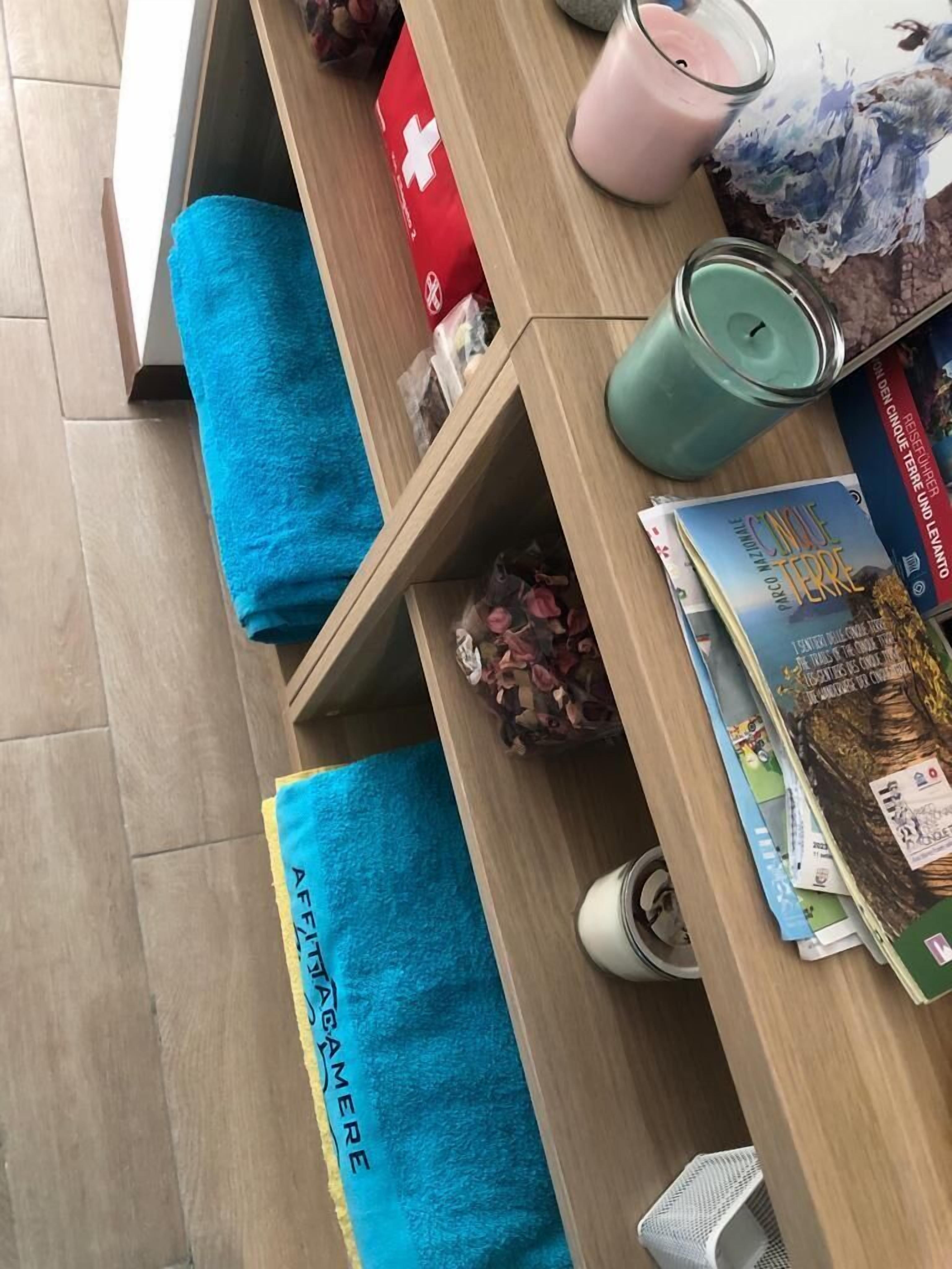 A wooden desk with a blue towel, a pink candle, and a green candle. There are books and a glass jar on the desk.