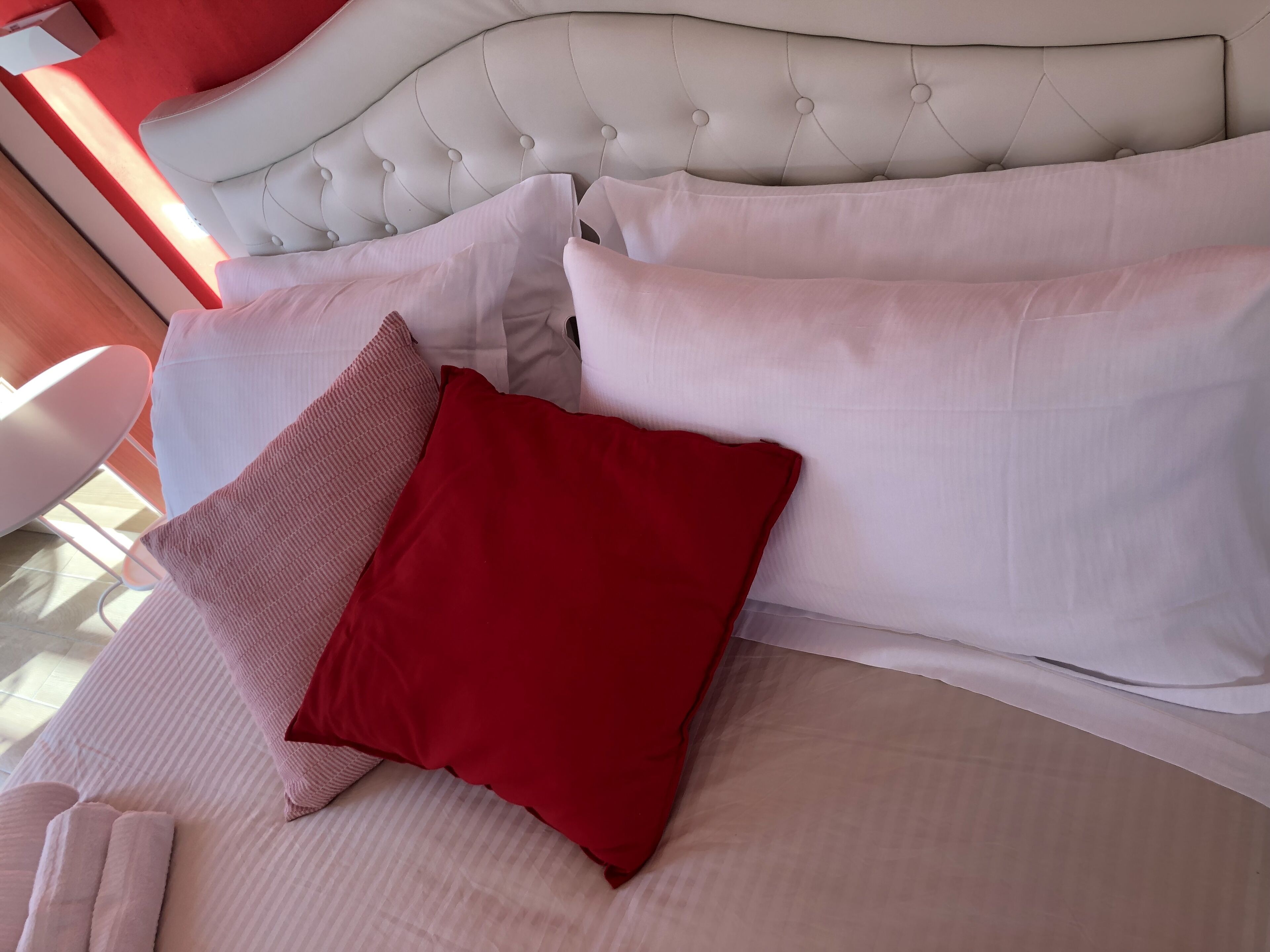 A bed with white and red pillows, a tufted headboard, and a white chair.