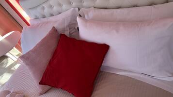 A bed with white and red pillows, a tufted headboard, and a white chair.