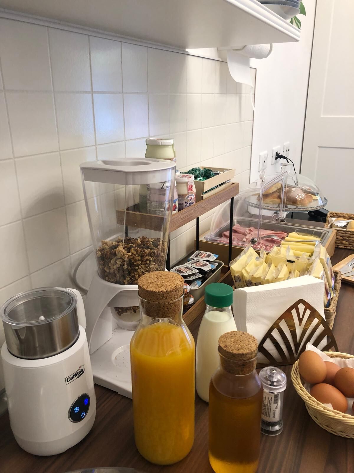 Una encimera de cocina con una cafetera, un extractor de zumos y diversos alimentos como pan, queso y huevos.