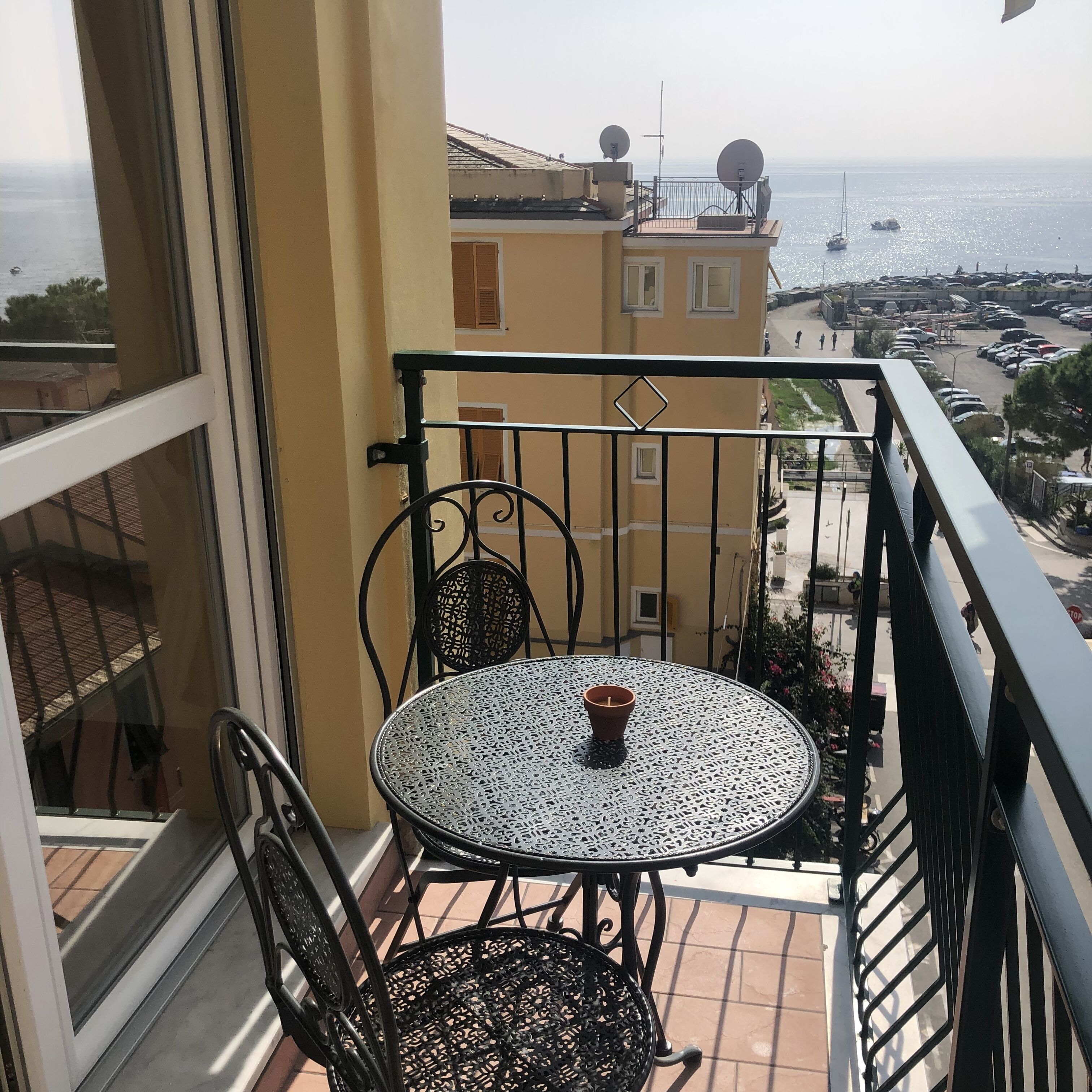 Een balkon met een ronde tafel en twee stoelen, met uitzicht op een jachthaven met boten en een parkeerplaats.