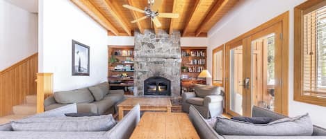 A living room with a stone fireplace, wooden ceiling beams, and a ceiling fan.
