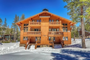 Eine mehrstöckige Holzhütte mit Steinunterbau, Balkonen und einer Treppe, die zum Eingang führt.