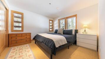 Une chambre à coucher avec un lit, une commode, une table de chevet, une lampe et des fenêtres.