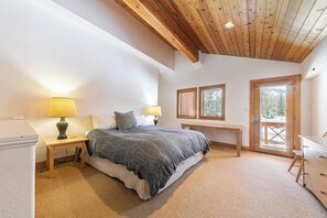 A bedroom with a bed, bedside lamps, a wooden bench, a dresser, and a door with a view.
