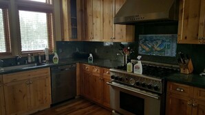 Une cuisine avec des meubles en bois, une cuisinière en acier inoxydable et une fenêtre équipée de stores.