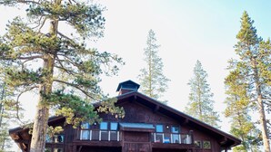 Un chalet à deux étages, avec une façade en bois, de nombreux balcons et un escalier menant à l’entrée.