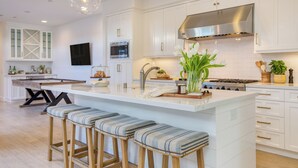 A modern kitchen with white cabinetry, a stainless steel range hood, a built-in microwave, and a large island with bar stools. - Stunning 5bdr Minutes to Beach, Pier, Restaurants Emerald Cove by Avantstay (Newport Beach)
