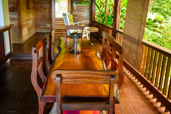 A wooden deck with a dining table and chairs, surrounded by a wooden railing and lush greenery.