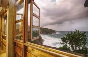 A room with a large window overlooking a coastal view with waves and a hilly landscape.