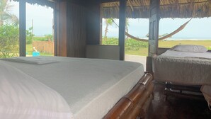 Una stanza con un letto, un'amaca e vista sulla spiaggia.