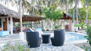 Zona junto a la piscina con sillones de descanso, una estructura de techo de paja y una piscina con azulejos.