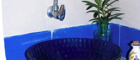 A bathroom with a blue sink, a white mirror with decorative molding, a potted plant with pink flowers, and a small decorative vase.