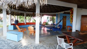 Un área de estar al aire libre cubierta con techo de paja, muebles azul y naranja, y una hamaca.