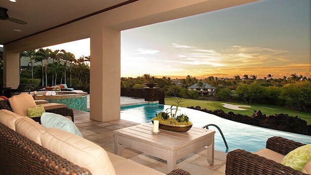 Zona de piscina con mobiliario de mimbre, una mesa blanca y vistas a un campo de golf y al atardecer.