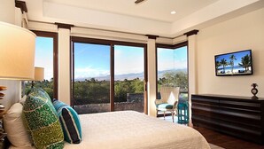 Un dormitorio con una cama grande, un ventilador de techo, un televisor en la pared y vistas al exterior.