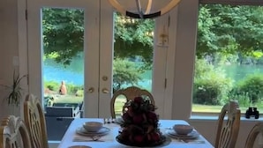 A dining room with a table set for six, a chandelier, and a view of a garden through large windows. - Luxury ocean dock pool villa (North Oyster)