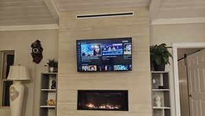 A living room with a flat-screen TV mounted above a fireplace, a clock on the wall, and a potted plant. - Luxury ocean dock pool villa (North Oyster)