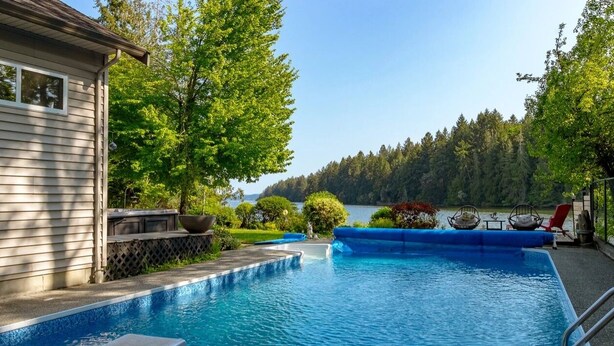 A swimming pool with a view of a forest and a lake, surrounded by a deck with outdoor furniture. - Luxury ocean dock pool villa (North Oyster)