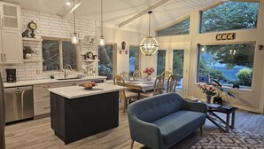 A modern kitchen with a central island, dining area with a table and chairs, and large windows offering a view of the outdoors. - Luxury ocean dock pool villa (North Oyster)