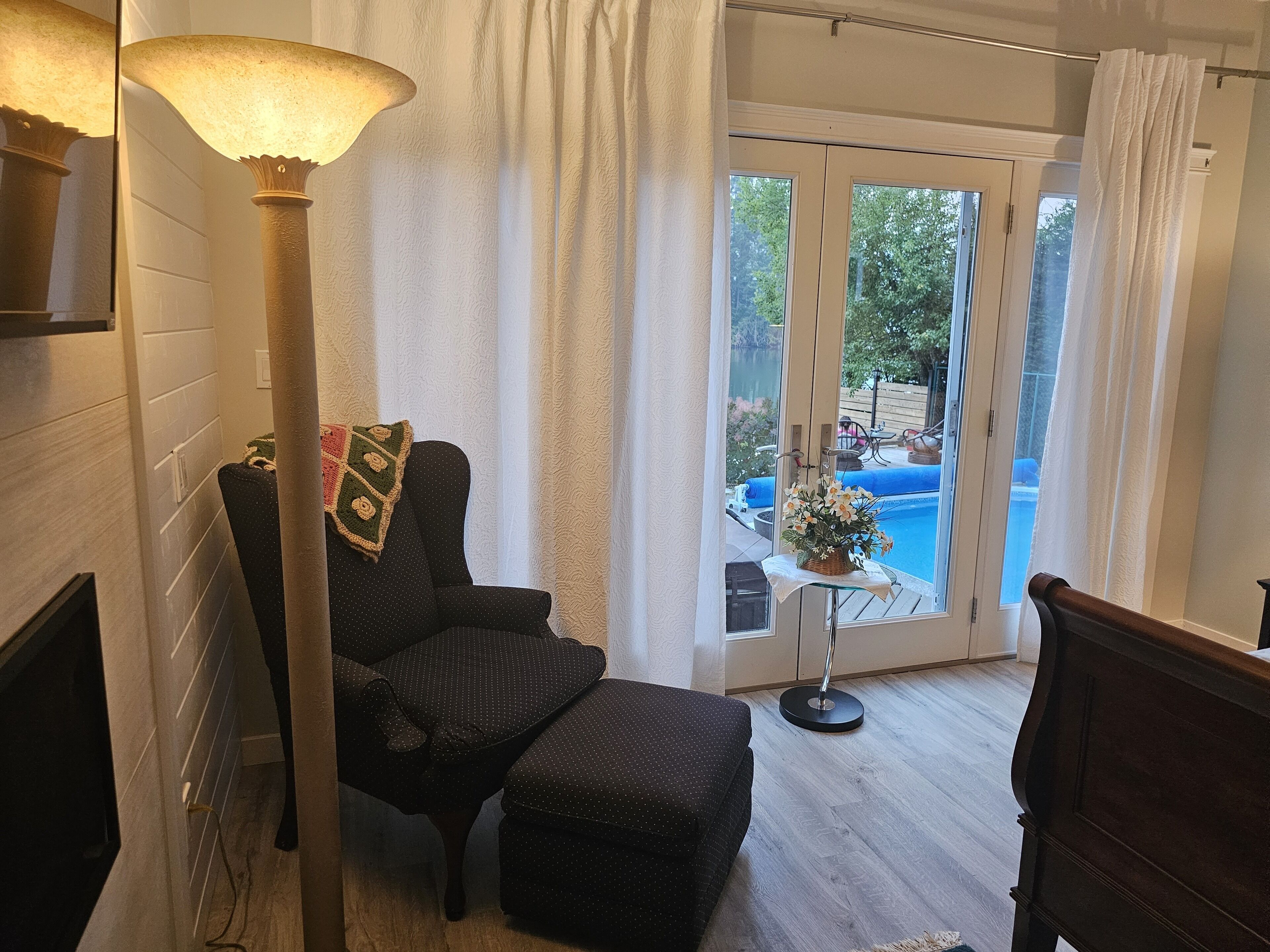 Sala de estar con un sofá de color oscuro, una lámpara de pie y vistas a una piscina a través de amplios ventanales.