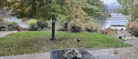 A deck with a square table, a bird feeder, and a view of a lake and trees.