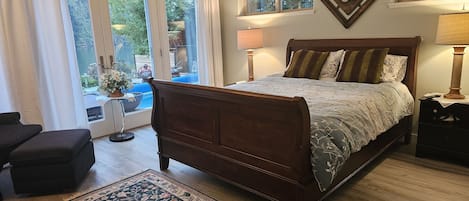 Une chambre à coucher avec un lit en bois, une table de chevet, une lampe, une fenêtre donnant sur un paysage verdoyant et un tapis à motifs.