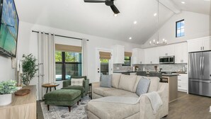 A modern living room with a sectional sofa, a small coffee table, and a TV. There is a kitchen area with white cabinets and stainless steel appliances. - Rise & Wine | Hot Tub | Sleeps 4 (Fredericksburg)
