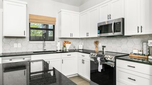 A modern kitchen with white cabinets, a black countertop, a stainless steel oven, and a microwave. - Rise & Wine | Hot Tub | Sleeps 4 (Fredericksburg)